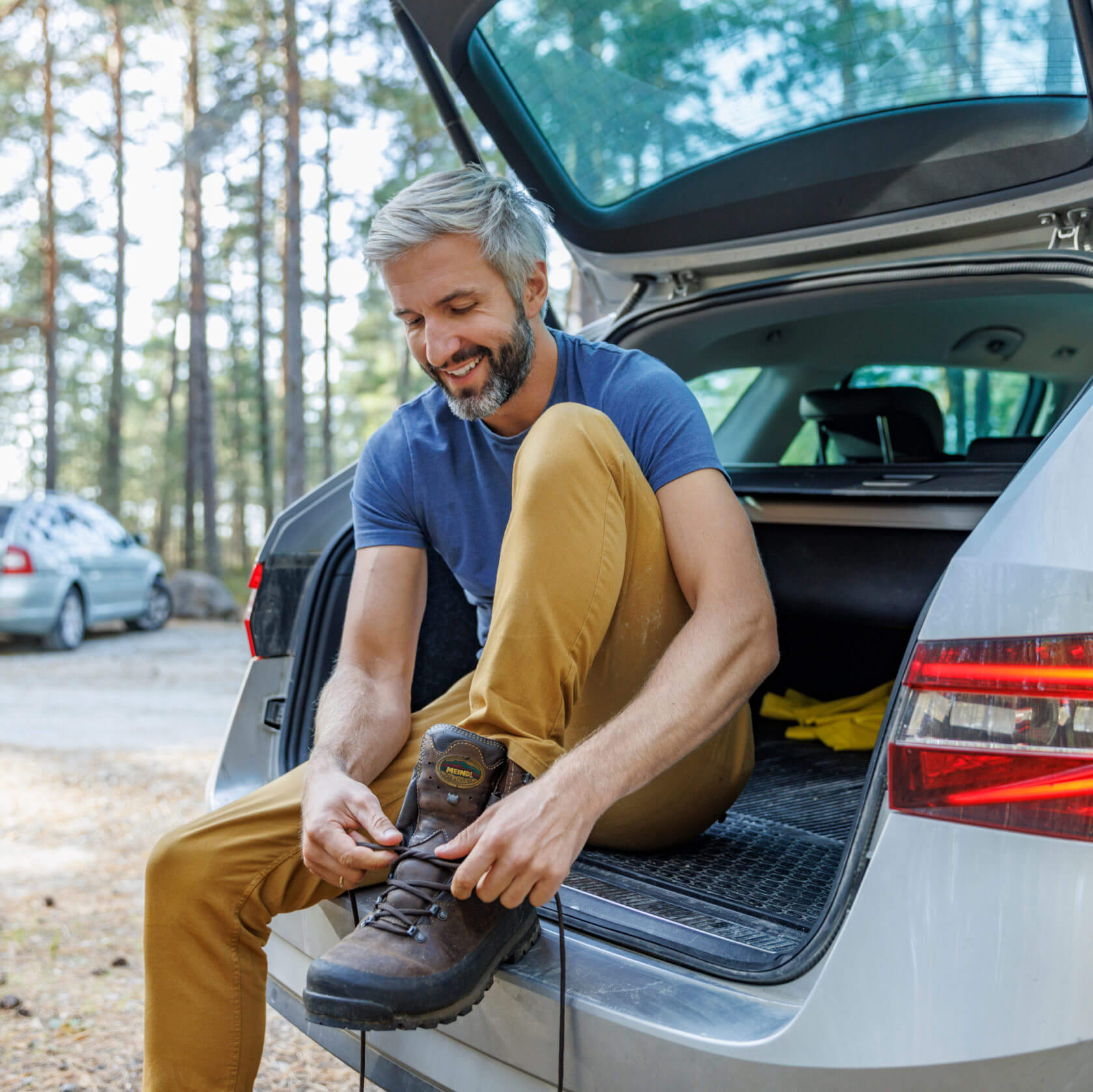 A person sitting on the boot of their car, tying shoelaces after a hike
